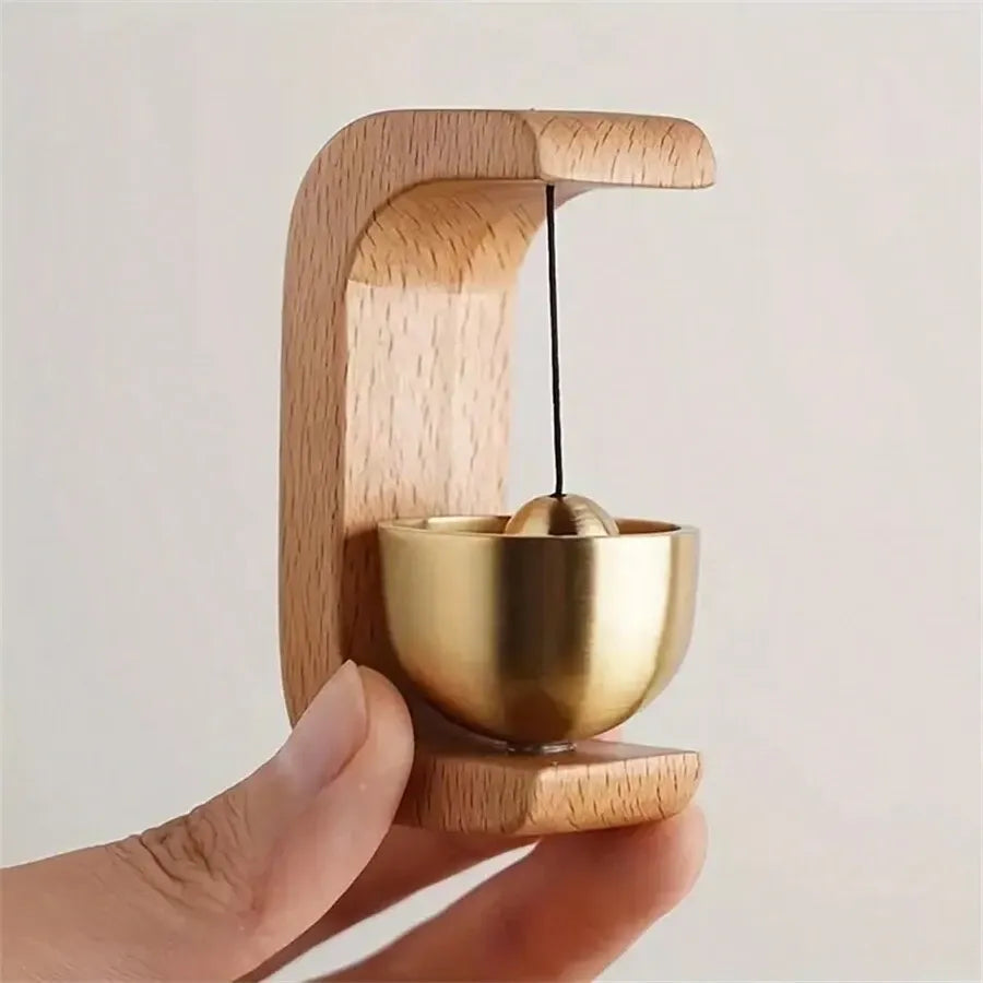 Hand holding wooden bell holder with brass singing bowl, minimalist home decor accent