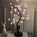 Glowing pink cherry blossom tree lamp with black branches, perfect for cozy bedroom or desk decor.